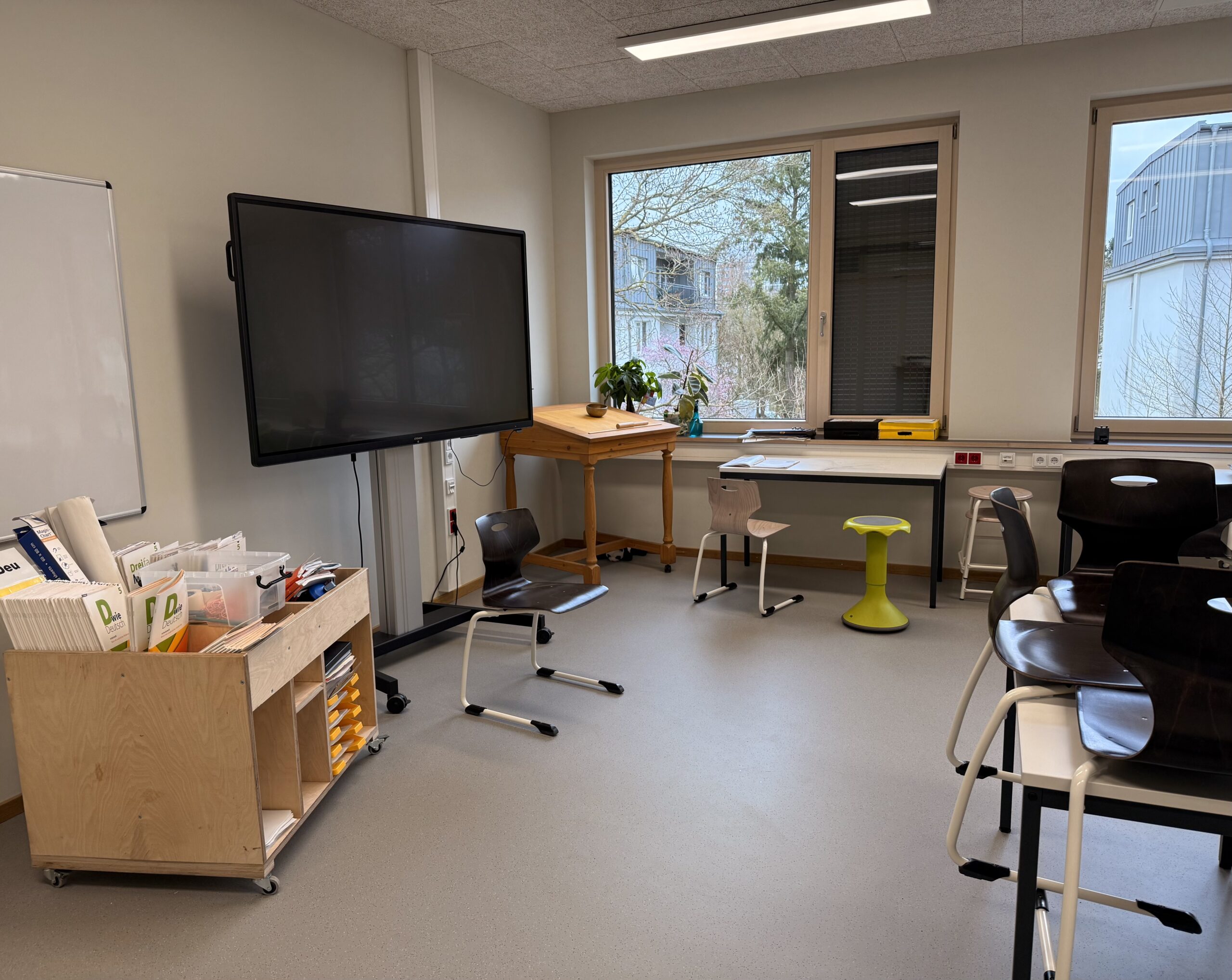 Klassenzimmer mit Bildschirm und Sitzgelegenheiten an Tischen